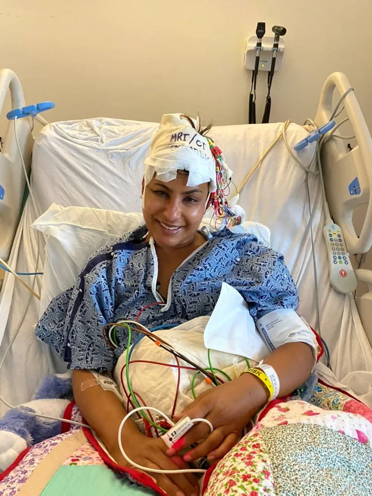 Charu Raheja in a hospital bed after her stroke, smiling, wired for monitoring