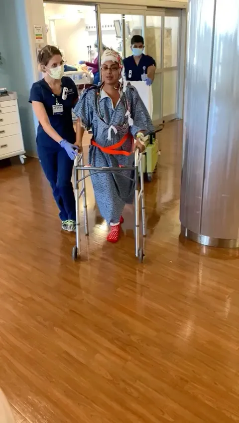 Charu Raheja walking out of the hospital with a walker, a nurse at her side